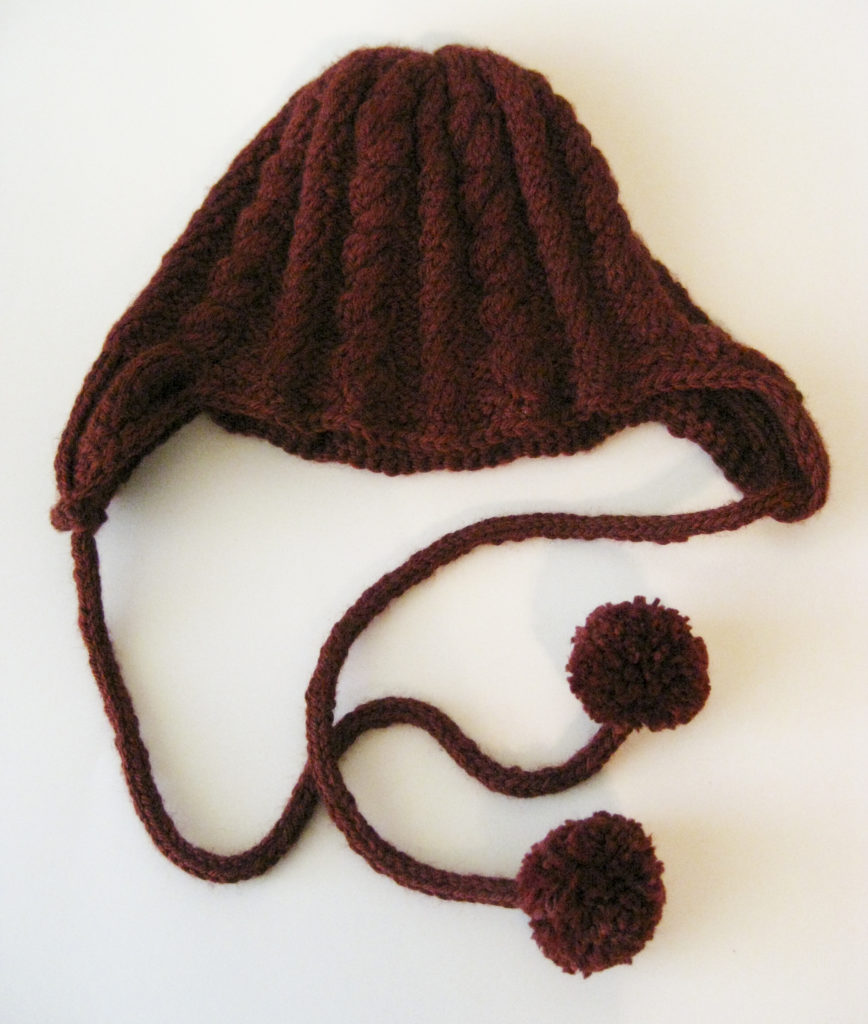 A cabled earflap hat with pom pom ties