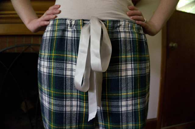 Close-up of tartan pajama pants waistband, which is held up with a silver satin ribbon tied in a bow