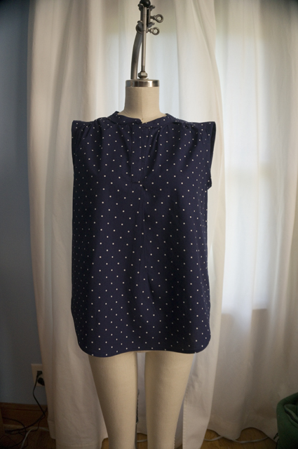 The front of a woman's sleeveless summer top with a half placket and curved hem