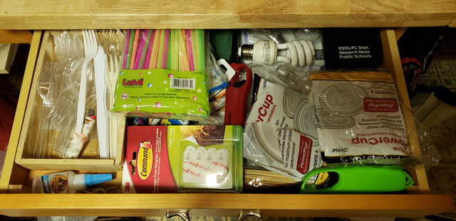 A drawer overflowing with plastic cutlery, drinking straws, lighters, adhesives, and other household ephemera