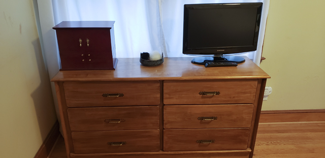 A wooden dresser, surmounted by a TV, jewelry chest, and small bowl of keychains, with an otherwise clean surface