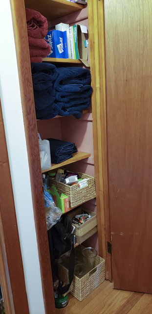 The inside of a closet containing shelves full of towels, boxes, and baskets before being organized