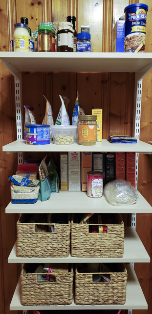 A freestanding pantry shelf unit neatly organized into groups of condiments, breakfast foods, grains and pastas, and sweet and salty snacks