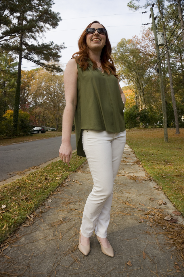 Caitlyn is standing on residential sidewalk wearing a sleeveless summer blouse, white jeans, nude pumps, and sunglasses