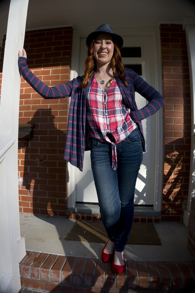 Caitlyn stands on her front porch smiling and wearing a denim hat, open-front cardigan, tie-front button-up shirt, jeans, and pointed-toe flats