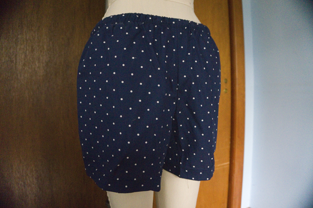 The back of a pair of drawstring pajama shorts hanging on a dress form