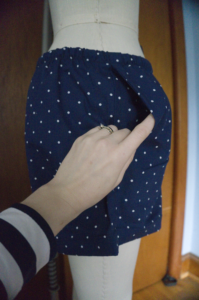 A close-up of the pocket opening in a pair of drawstring pajama shorts hanging on a dress form