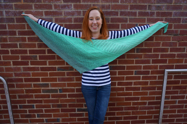 Caitlyn holds up a shawl made with Freia Handpaints yarn to show the full wingspan and different lace patterns