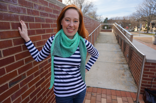 Caitlyn stands with one hand on a brick wall and her lace shawl wrapped around her neck like a bandana