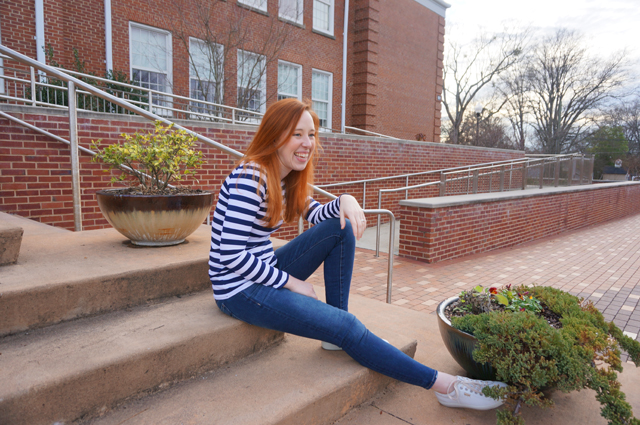 Caitlyn is wearing a long-sleeve striped t-shirt she made, sitting on the steps of a public building, and laughing at something off-camera