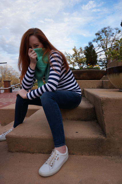 Caitlyn sits on the steps of a public building and peers playfully from behind her bandana shawl