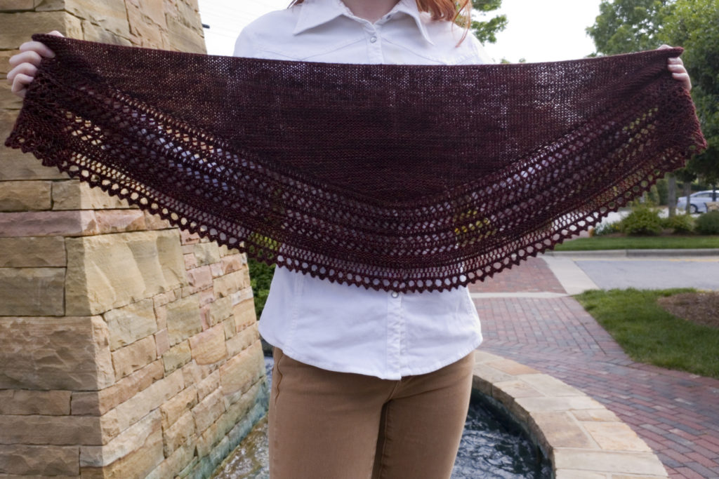 A close-up of Caitlyn holding the Henslowe shawl to show the shape is a shallow, rounded triangle