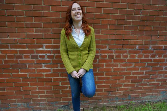 Caitlyn is leaning against a brick wall and wearing her CustomFit Stonington cardigan by Amy Herzog