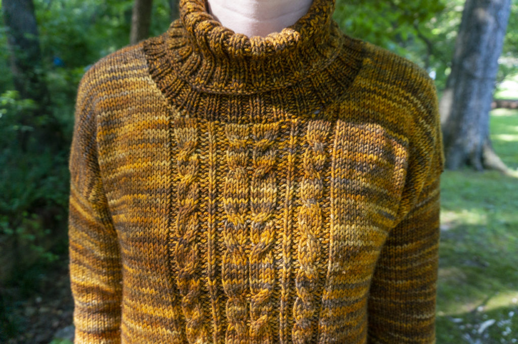 A golden-brown sweater with a central cable panel, turtleneck, and long sleeves