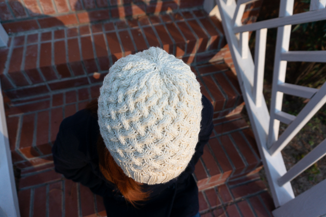 A top-down view of cable knit hat in off-white yarn being worn on the head