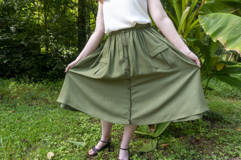 A sage green below-the-knee button-front skirt with a gathered waist and patch pockets